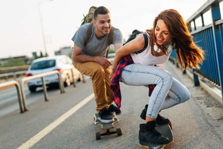 Portrait of happy couple having fun while driving a long board in city. People skateboard conceptの写真素材