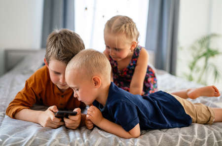 Portrait of children playing on mobile phone together at home. Internet and network addiction.の写真素材