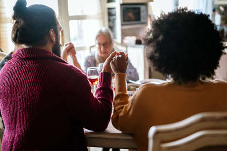Multiethnic family saying prayer before eating meal at home togetherの写真素材
