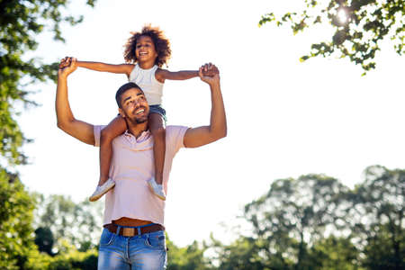 Portrait of happy black father carrying daughter on back outdoors. Family happiness love concept.の写真素材