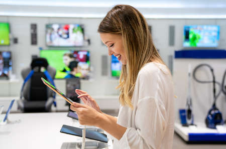 Beautiful young woman choosing which digital device to buy in tech store..
