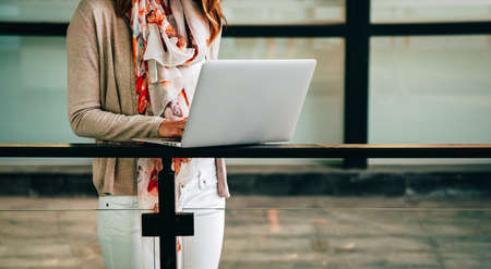 Confident young woman working on laptop while sitting near window in creative office or cafeの写真素材