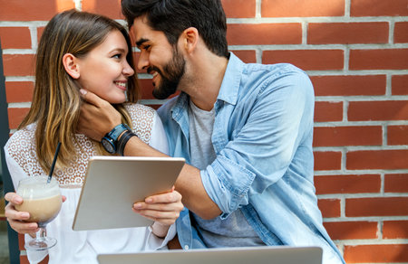 Couple sitting at cafe smiling, using laptop, spending time with pleasure, drinking coffee.の写真素材