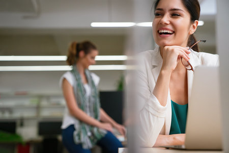 Successful young businesswoman working on laptop in office with colleagues at the background.の写真素材