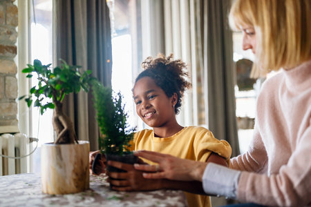 Happy caucasian mother and her adopted african american daughter taking care of plants indoors.の写真素材