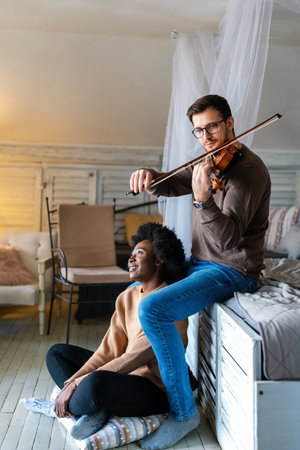 Multiethnic couple is spending romantic moments together. Man playing the violin for his girlfriendの写真素材