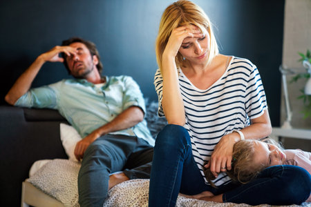 Tired mother and father sitting on couch feels annoyed exhausted stressful with little girl child.の写真素材