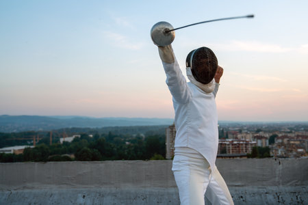 Woman in white fencing costume practicing outdoors. Sport, professional coach, healthy lifestyle.