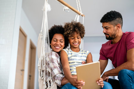 Happy african family having fun with device at home, using digital tablet looking at screen togetherの写真素材