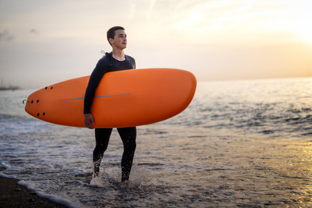 Joyful youngoman carrying a surfboard on a beach, his face filled with happiness and excitementの写真素材