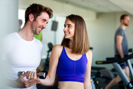 Handsome man personal trainer helping fit woman working with dumbbells in fitness gym club