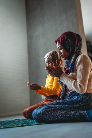 Beautiful muslim mother and child performing islamic prayers