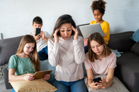 Sad woman with multiethnic children using digital gadgets.. Family and modern technology addiction.