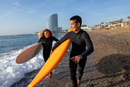 Beautiful happy surfer couple having fun on the beach, running with surfboard to the wavesの写真素材