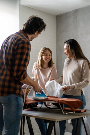 Happy mixed race family doing together domestic chores, ironing, household together at home.