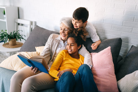 Happy grandmother having fun, reading book to multiethnic grandchildren.の写真素材