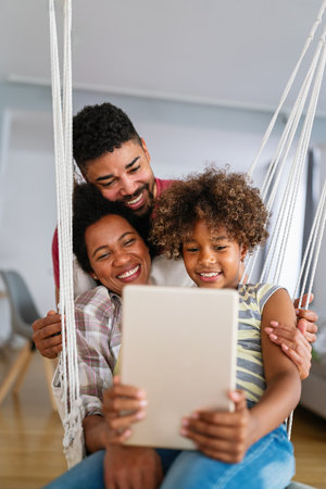 Happy african family having fun with device at home, using digital tablet looking at screen togetherの写真素材