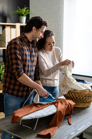 Happy young mixed race couple doing the ironing together at homeの写真素材