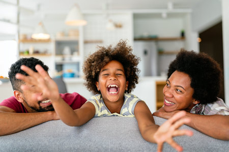 Happy biracial girl smiling with young multiracial parents enjoy weekend at home together,の写真素材