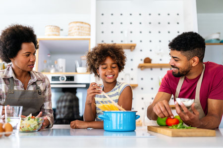 Happy african american family preparing healthy food in kitchen, having fun together on weekendの写真素材