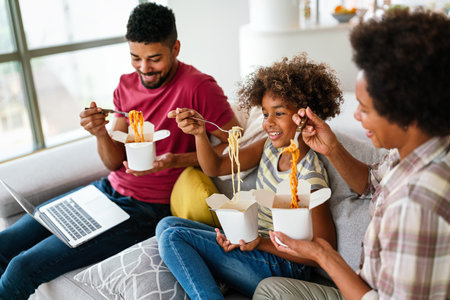 Happy african family eating at living room and enjoying time together. Home delivary takeaway foodの写真素材
