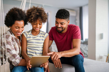 Planning vacation together. African american father, mother and daughter using tablet at home,の写真素材