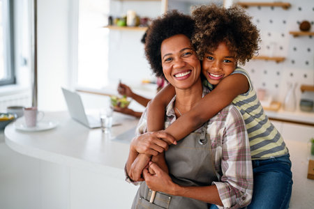 Portrait of happy black woman and her cute preteen daughter having fun together at homeの写真素材
