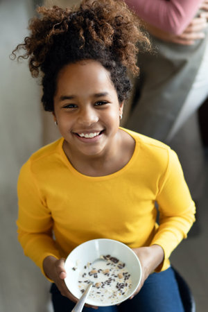 Happy african american child girl having breakfast eating cereal in kitchen.の写真素材