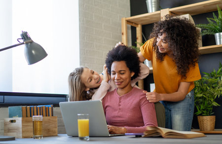 Black mother using computer and trying to focus on work while her children disturb herの写真素材
