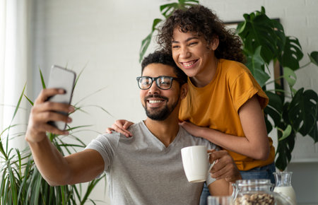 Joyful couple smiling and taking selfie on cellphone while having breakfast at homeの写真素材