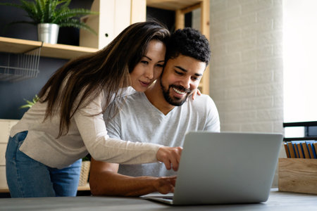Happy interracial couple smiling while working or having fun at laptopの写真素材