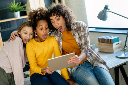 Happy multiethnic teenagers holding technology gadgets using digital devices studying together.の写真素材