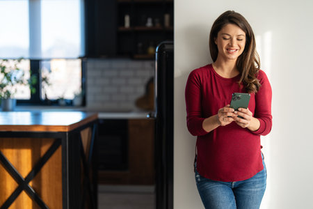 Happy relaxed young pregnant woman using cell phone, smiling lady laughing holding smartphoneの写真素材