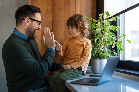 Fatherhood and remote business. Happy young single dad working at home while child plays next to himの写真素材