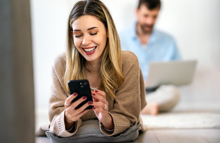 Smiling young woman chatting in social networks, working, using mobile applications at home.の写真素材