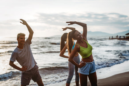 Group of young people, friends in sports clothing jogging while exercising on the beach outdoors