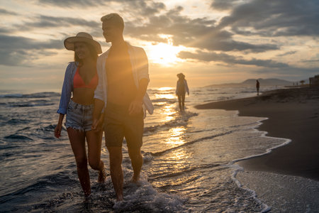 Happy young casual couple holding hands and walking at the beach, enjoying summer vacationの写真素材