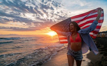 Young woman holding national American flag walking ocean beach. America Independence Day conceptの写真素材