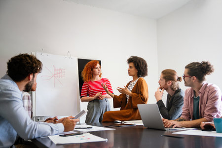 Diverse group of happy employees analyzing reports with digital device, working together in officeの写真素材