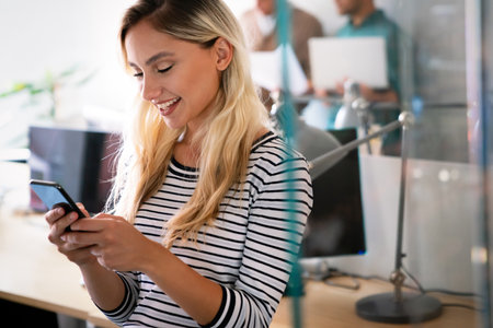 Smiling caucasian businesswoman watching on smartphone during work at office.の写真素材