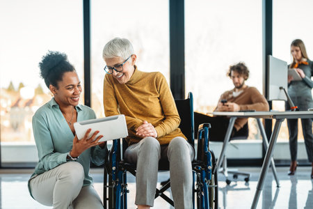 Disabled woman in wheelchair looking at computer, discussing startup project with interracial teamの写真素材