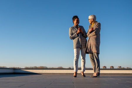 Two diverse business woman holding cup of coffee outdoors. Business woman talking for business planの写真素材