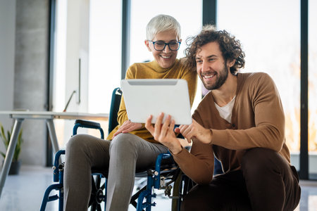 Business woman in wheelchair working with colleague in modern inclusive office. Diversity, supportの写真素材