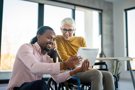 Disabled woman in wheelchair looking at computer, discussing startup project with interracial teamの写真素材