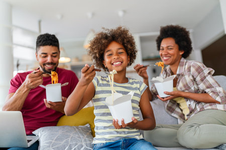 Happy african family eating at living room and enjoying time together. Home delivary takeaway foodの写真素材