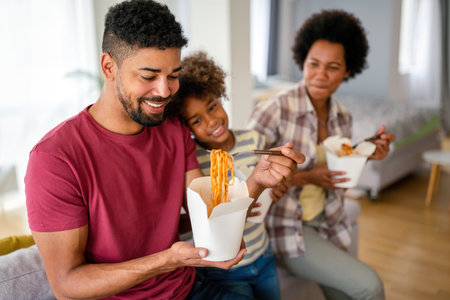 Happy african family eating at living room and enjoying time together. Home delivary takeaway foodの写真素材