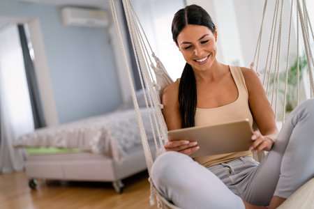 Happy beautiful woman watching videos or enjoying entertainment content on a tablet at homeの写真素材