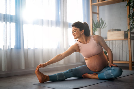 Charming pregnant fit woman in leggings and crop top exercising on yoga mat in living-room.の写真素材