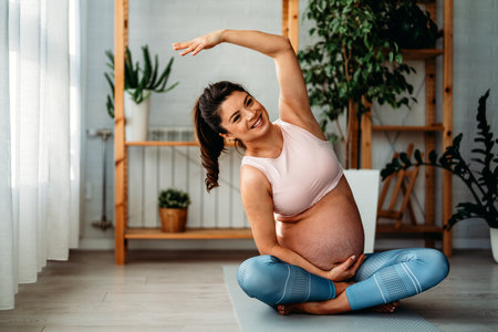 Portrait of young pregnant female working out at home. Pregnant woman practicing yoga at home.の写真素材