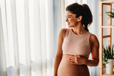 Fit pregnant woman holding hands on her belly, enjoying in the last trimester of pregnancy.の写真素材